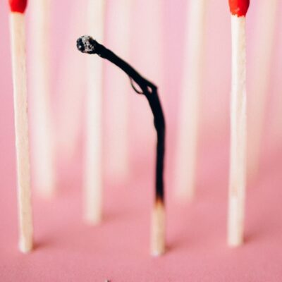 Close-up of a burnt matchstick amidst unburned ones on a pink surface, symbolizing uniqueness.